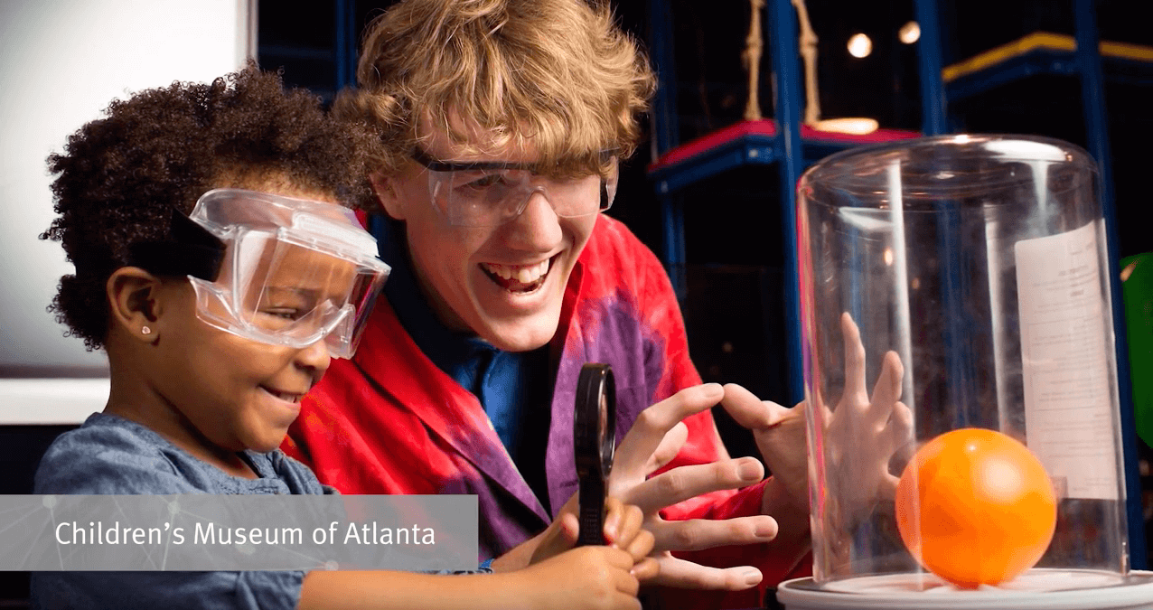 A child and caregiver wearing goggles and doing a science experiment at a children's museum