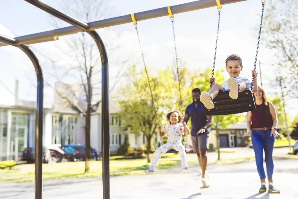 caregivers pushing children on swings at a playground