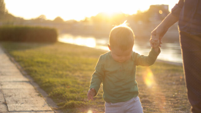 Young child walking, looking down, and holding caregivers hand.