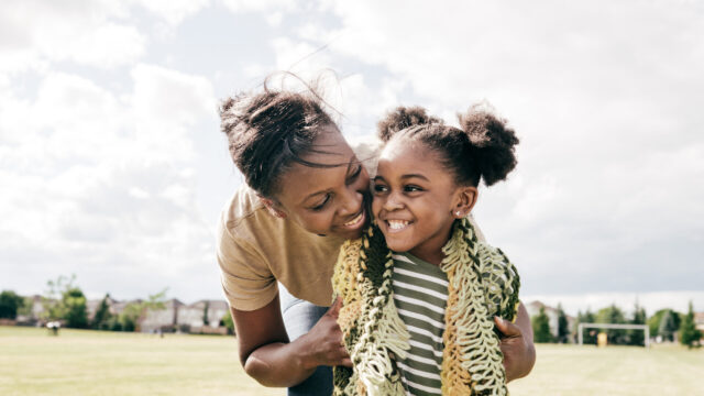 Caregiver and young child smiling at each other at park