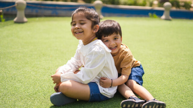 Two young child hugging, sitting on grass.