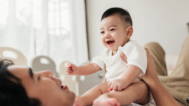 Baby sitting on caregiver, laughing