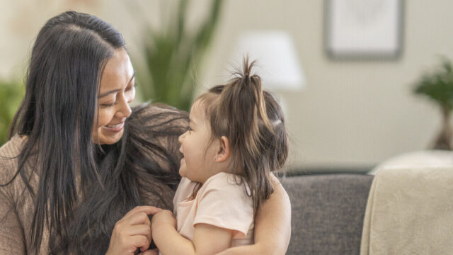 Caregiver holding child on couch, both laughing at each other