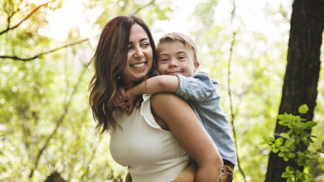 Young child outside riding on caregiver's back, smiling