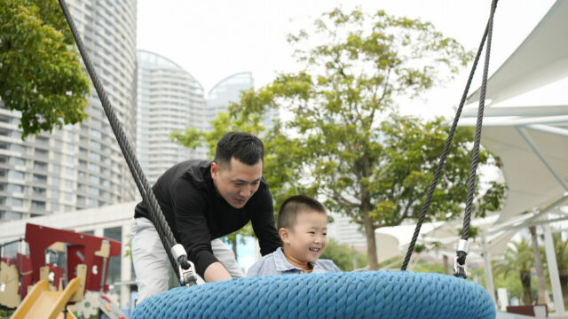 Caregiver pushing toddler on a swing in a city