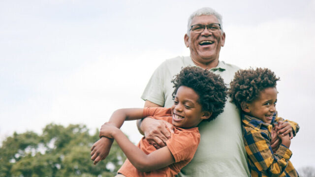 Caregiver swinging two young children, all laughing.