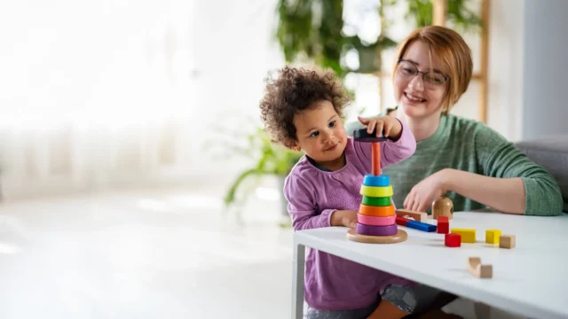 caregiver playing with child and blocks at table.